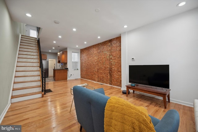 living room with stairway, light wood finished floors, brick wall, baseboards, and recessed lighting