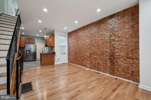 unfurnished living room with light wood-style flooring, visible vents, stairway, and brick wall