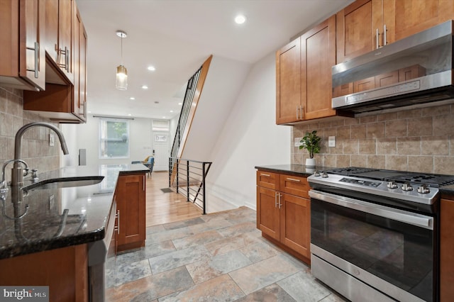 kitchen with backsplash, stainless steel gas range oven, hanging light fixtures, and sink