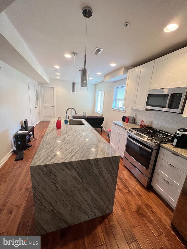 kitchen with white cabinets, an island with sink, stainless steel appliances, and dark hardwood / wood-style flooring