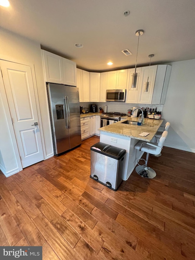 kitchen with white cabinets, kitchen peninsula, decorative light fixtures, hardwood / wood-style flooring, and stainless steel appliances