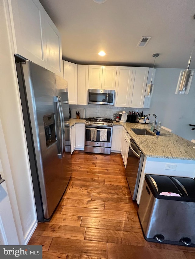 kitchen featuring white cabinets, kitchen peninsula, decorative light fixtures, light hardwood / wood-style flooring, and stainless steel appliances