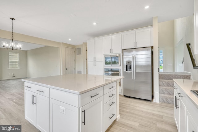 kitchen with a center island, hanging light fixtures, stainless steel appliances, white cabinets, and light hardwood / wood-style flooring