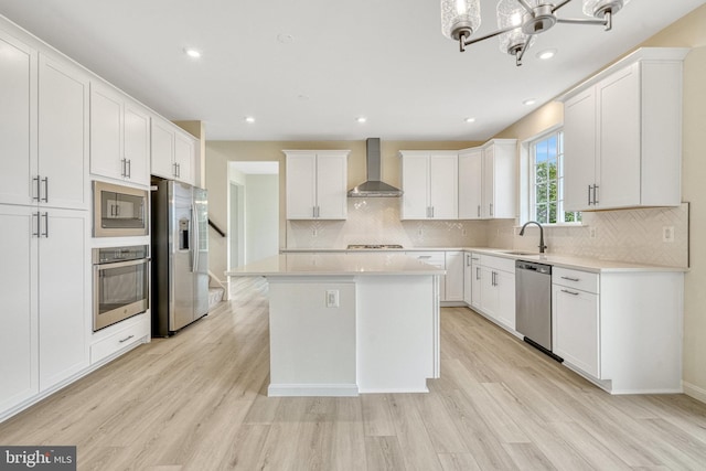 kitchen featuring light hardwood / wood-style floors, wall chimney exhaust hood, appliances with stainless steel finishes, and white cabinets