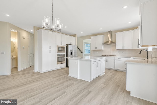 kitchen with light wood finished floors, decorative backsplash, appliances with stainless steel finishes, wall chimney exhaust hood, and a sink