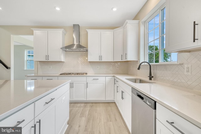 kitchen with wall chimney range hood, light countertops, stainless steel appliances, white cabinetry, and a sink