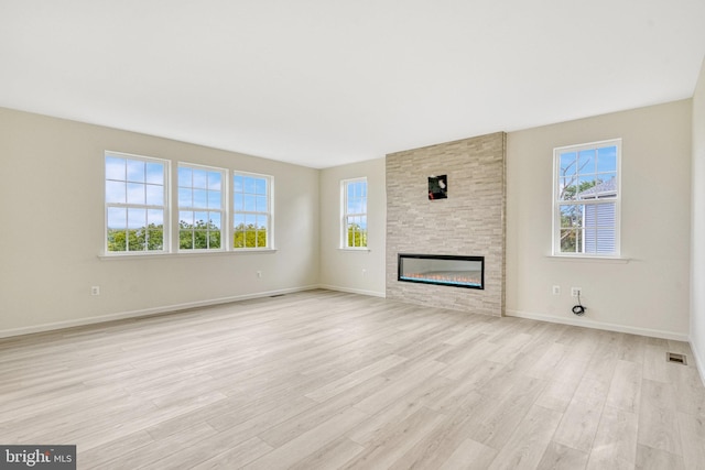 unfurnished living room featuring light wood-type flooring, plenty of natural light, visible vents, and a fireplace