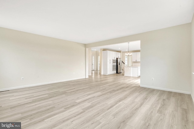 unfurnished living room with an inviting chandelier, light wood-style flooring, and baseboards