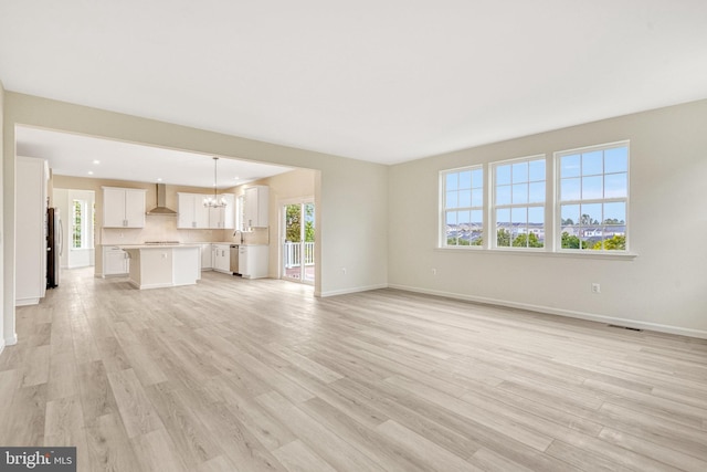 unfurnished living room featuring an inviting chandelier, light wood-type flooring, and plenty of natural light