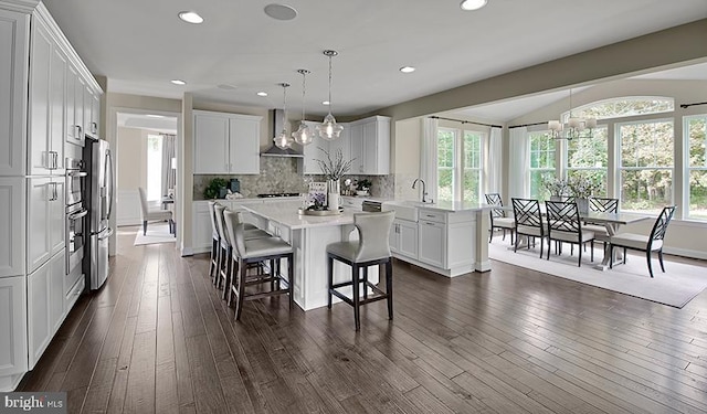 kitchen featuring dark wood-type flooring, stainless steel fridge with ice dispenser, a kitchen bar, light countertops, and wall chimney exhaust hood