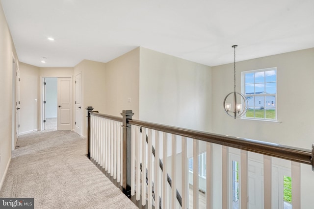 hallway with baseboards, carpet floors, an inviting chandelier, and an upstairs landing