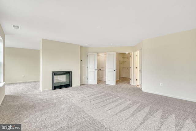 unfurnished living room featuring light carpet, a glass covered fireplace, baseboards, and visible vents