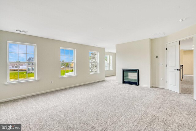 unfurnished living room featuring visible vents, baseboards, a glass covered fireplace, and carpet flooring