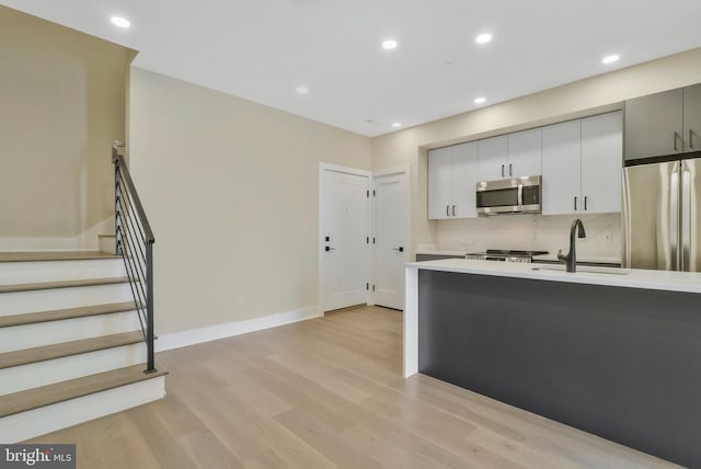 kitchen featuring appliances with stainless steel finishes, gray cabinetry, backsplash, light hardwood / wood-style flooring, and sink