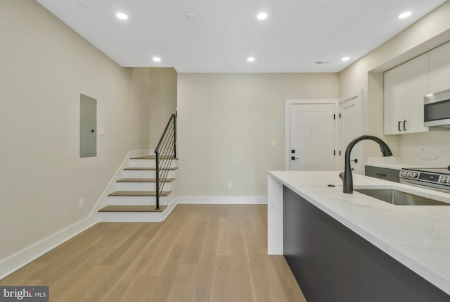 kitchen featuring light hardwood / wood-style flooring, white cabinets, light stone counters, and electric panel