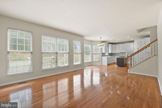 unfurnished living room with light wood-type flooring, plenty of natural light, and a chandelier