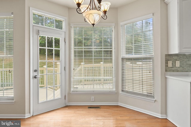 doorway to outside with a wealth of natural light, a chandelier, and light wood-type flooring