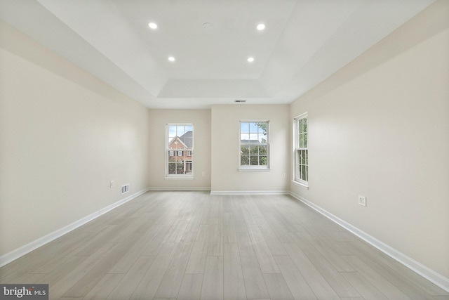 empty room featuring light wood-type flooring and a tray ceiling