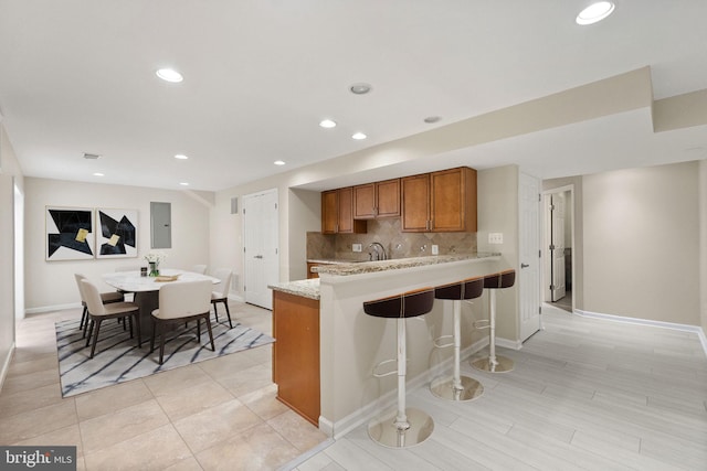 kitchen featuring electric panel, kitchen peninsula, tasteful backsplash, a kitchen breakfast bar, and light stone countertops