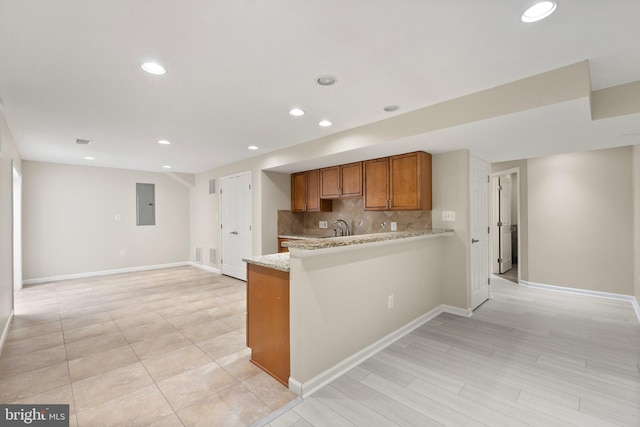 kitchen featuring electric panel, kitchen peninsula, sink, backsplash, and light stone countertops