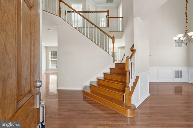 stairway featuring wood-type flooring, ornamental molding, a towering ceiling, and a chandelier