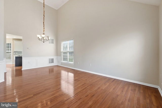 interior space featuring high vaulted ceiling, wood-type flooring, ornamental molding, and an inviting chandelier