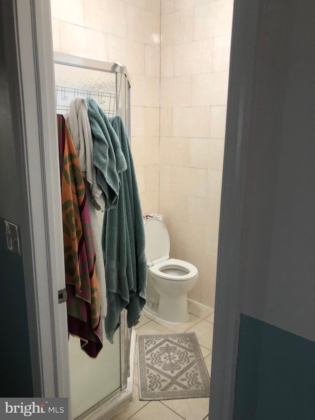 bathroom with a stall shower, toilet, tile patterned flooring, and tile walls
