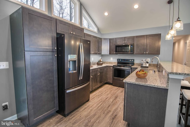 kitchen with pendant lighting, sink, stainless steel appliances, a kitchen bar, and kitchen peninsula