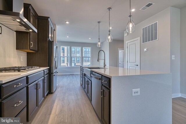 kitchen featuring a kitchen island with sink, light wood-type flooring, sink, and wall chimney range hood