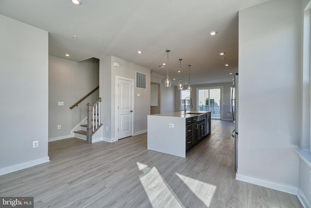 kitchen with light wood-type flooring, a kitchen island with sink, sink, and pendant lighting