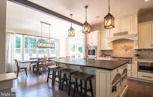 kitchen featuring a center island with sink, hanging light fixtures, dark hardwood / wood-style flooring, and tasteful backsplash