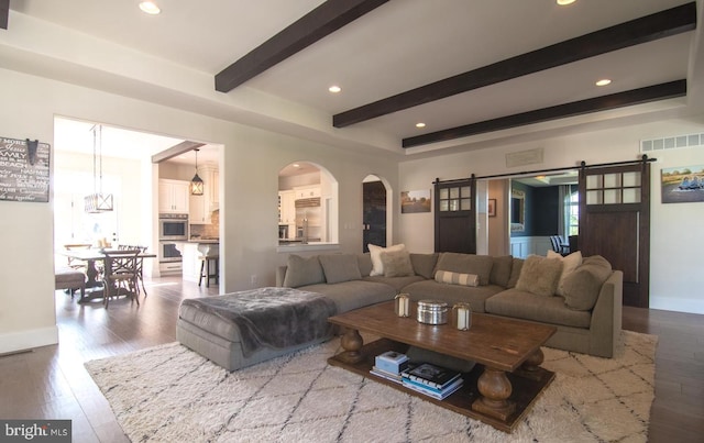 living room featuring beam ceiling, light hardwood / wood-style floors, and a barn door