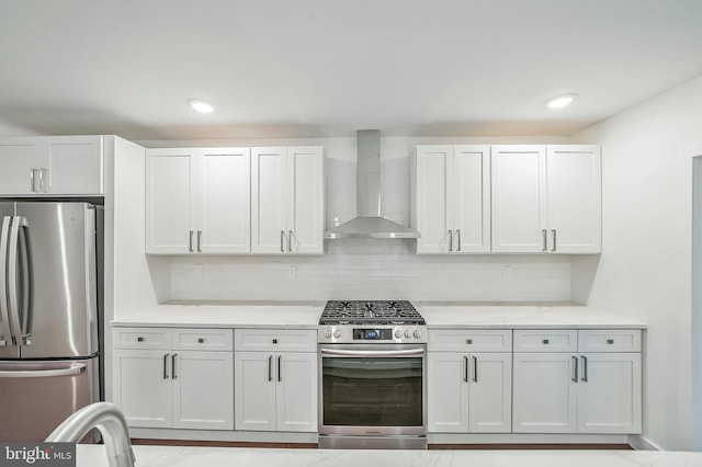 kitchen featuring light stone counters, wall chimney exhaust hood, stainless steel appliances, and white cabinets