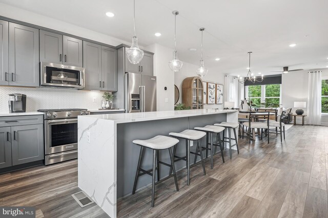 kitchen with appliances with stainless steel finishes, hanging light fixtures, light stone counters, dark hardwood / wood-style flooring, and a large island