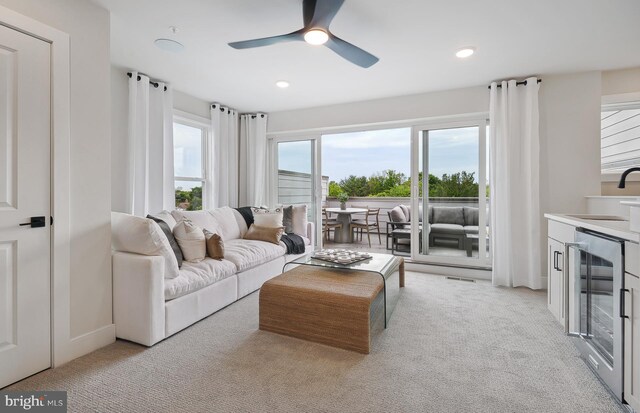 living room with beverage cooler, light carpet, sink, and ceiling fan