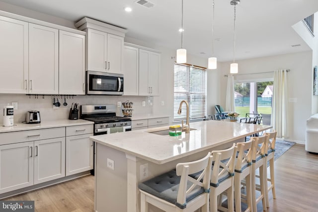 kitchen with appliances with stainless steel finishes, hanging light fixtures, a kitchen island with sink, and sink