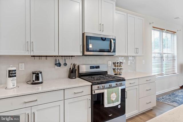 kitchen featuring appliances with stainless steel finishes, light hardwood / wood-style floors, white cabinetry, light stone counters, and tasteful backsplash