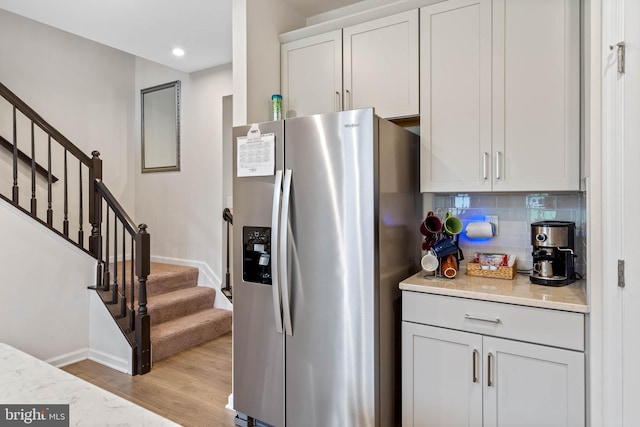 kitchen featuring stainless steel refrigerator with ice dispenser, light hardwood / wood-style floors, decorative backsplash, and white cabinetry