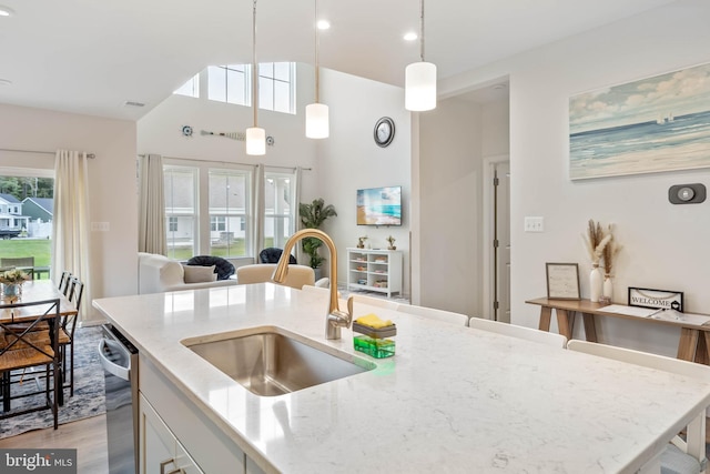 kitchen with light stone counters, sink, decorative light fixtures, light hardwood / wood-style flooring, and dishwasher