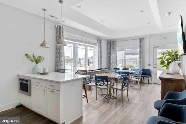 kitchen featuring decorative light fixtures, white cabinetry, a tray ceiling, stainless steel oven, and light wood-type flooring