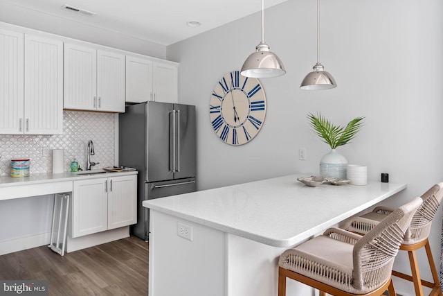 kitchen with white cabinets, hanging light fixtures, high end fridge, a breakfast bar area, and dark hardwood / wood-style flooring