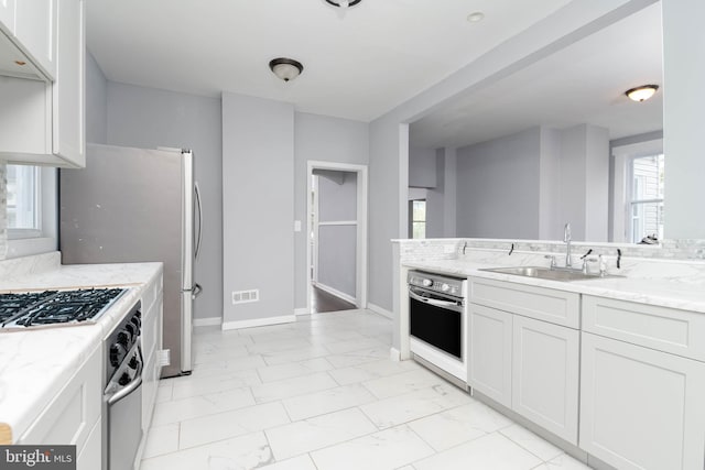 kitchen with light stone counters, appliances with stainless steel finishes, sink, and white cabinetry