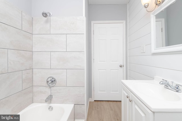 bathroom with wooden walls, hardwood / wood-style floors, tiled shower / bath combo, and vanity