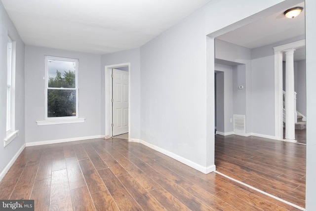 empty room with decorative columns and dark wood-type flooring