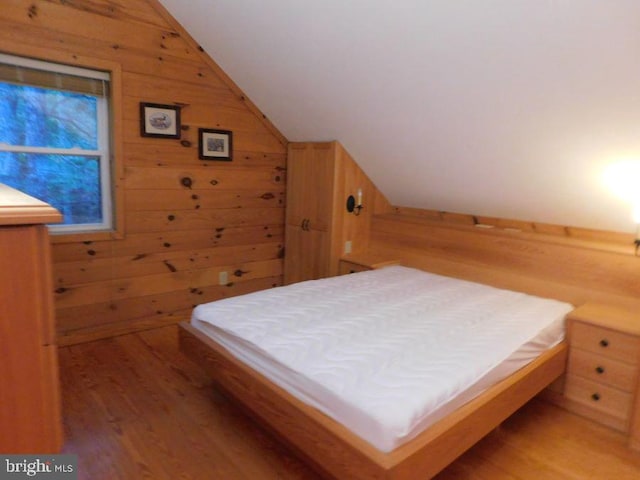 bedroom with vaulted ceiling, hardwood / wood-style flooring, and wood walls