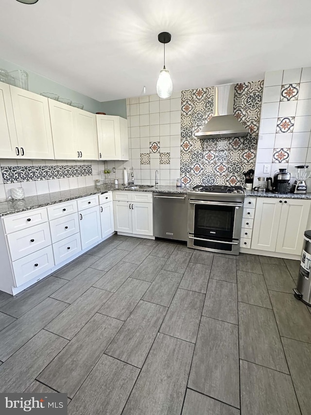 kitchen featuring backsplash, white cabinets, wall chimney exhaust hood, decorative light fixtures, and stainless steel appliances