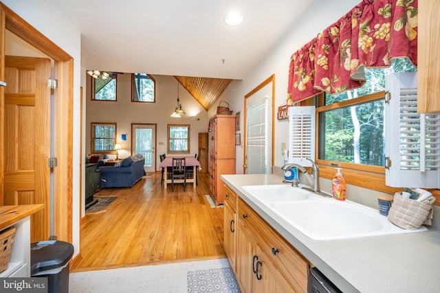 kitchen featuring light brown cabinets, light hardwood / wood-style floors, sink, decorative light fixtures, and vaulted ceiling