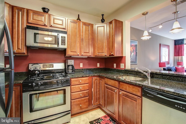 kitchen featuring pendant lighting, stainless steel appliances, dark stone counters, and sink