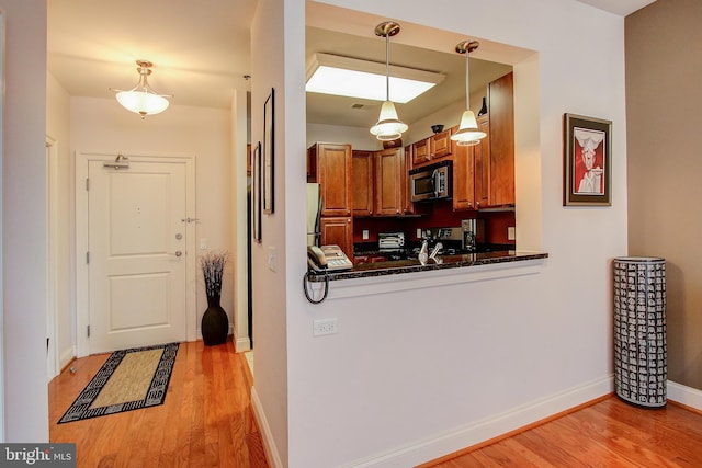 kitchen featuring pendant lighting, kitchen peninsula, appliances with stainless steel finishes, and light hardwood / wood-style flooring