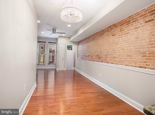 hall with wood-type flooring, a chandelier, and brick wall